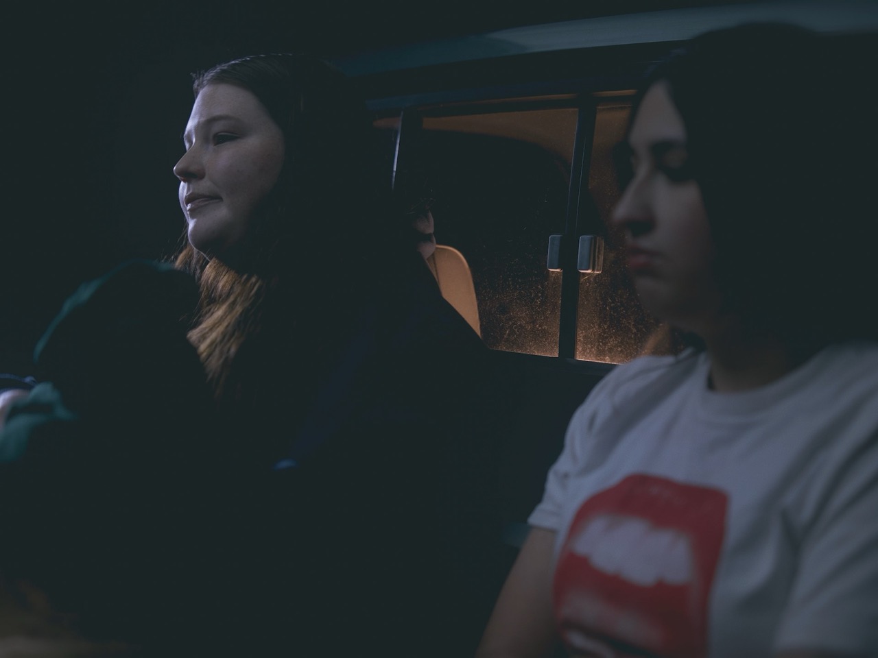 two young women sit in the bed of a truck in the dark of night