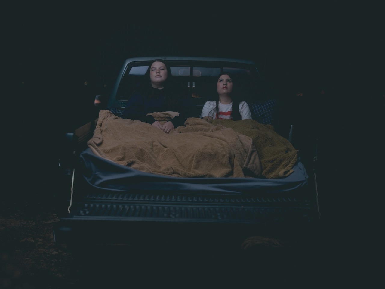 two young woman sit in the back of a truck in the dark of night