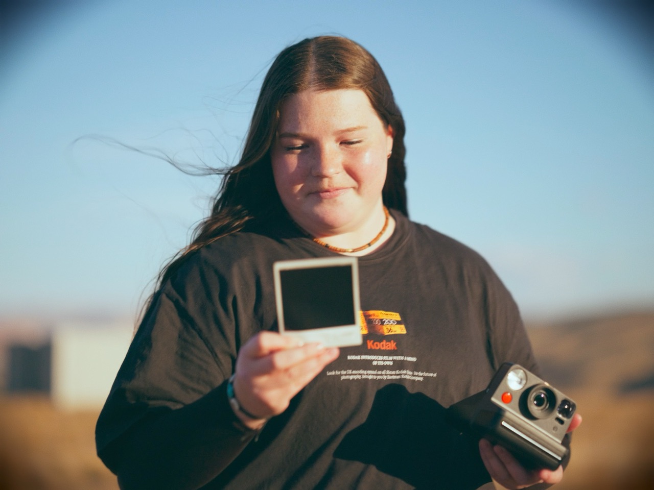 a woman looks at a polaroid in a bright field