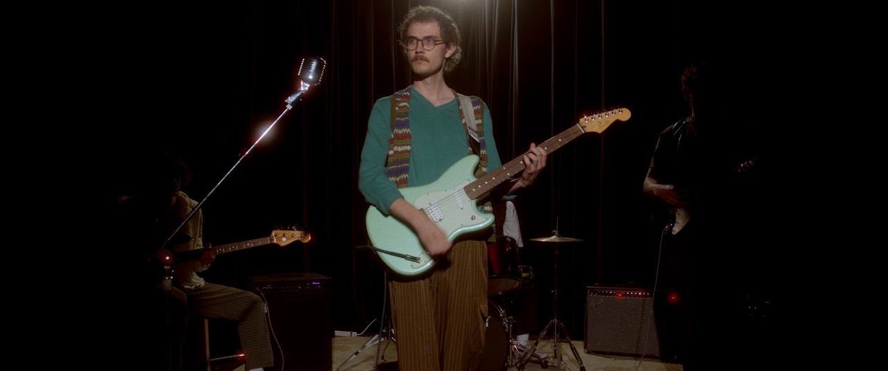 a man stands in a dark room with a guitar