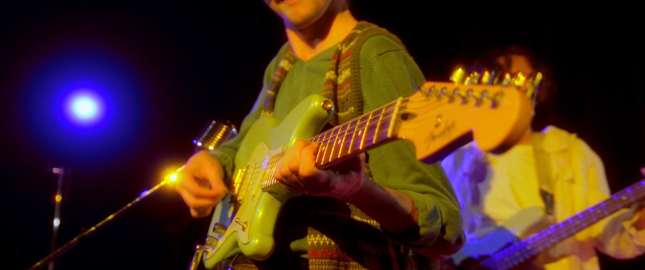 a man plays his guitar in a dark room lit with colored light