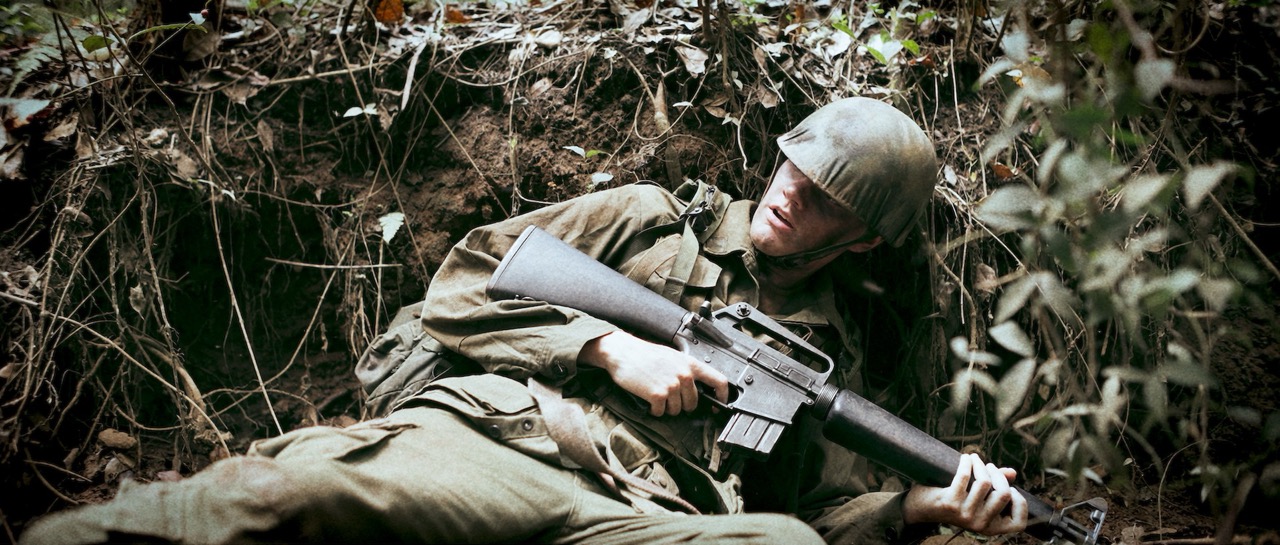 a man in a war uniform lays in a dark bush