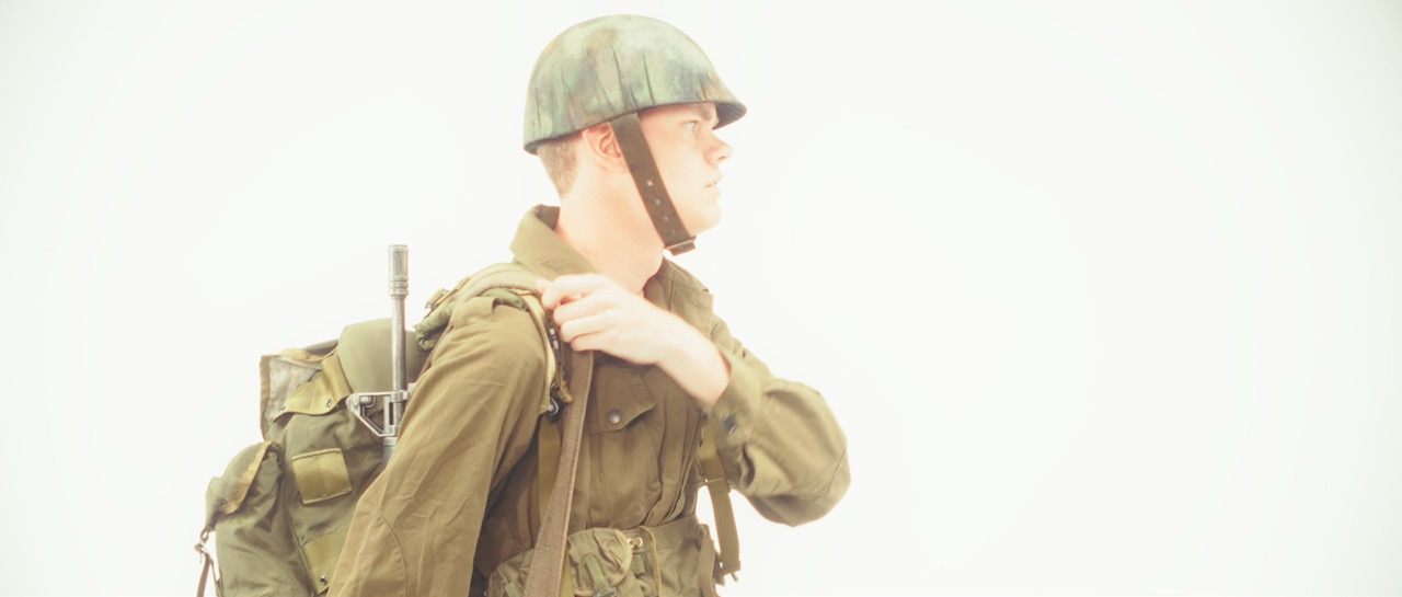 a man in a war uniform puts on his backpack in a white void
