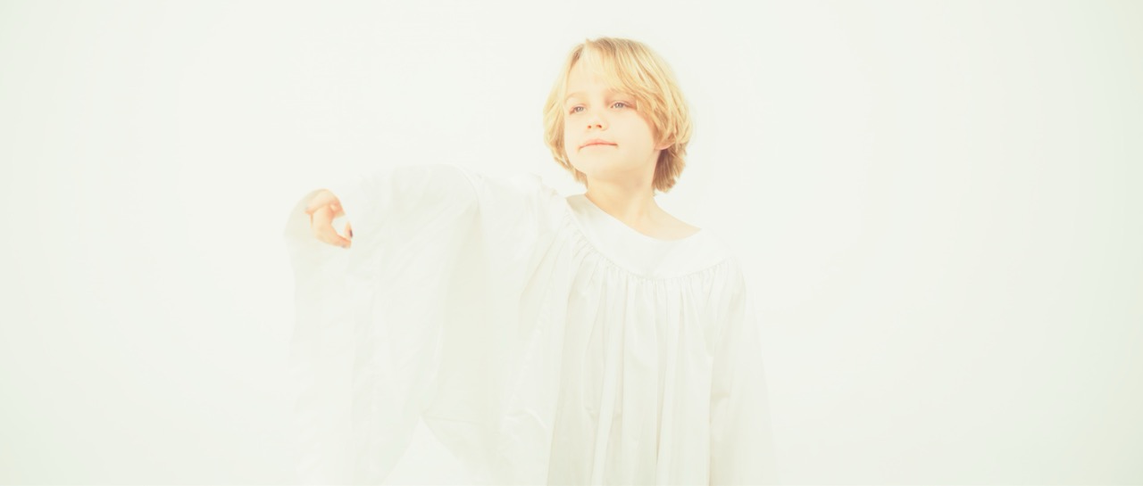 a young boy in a white robe points in a white void