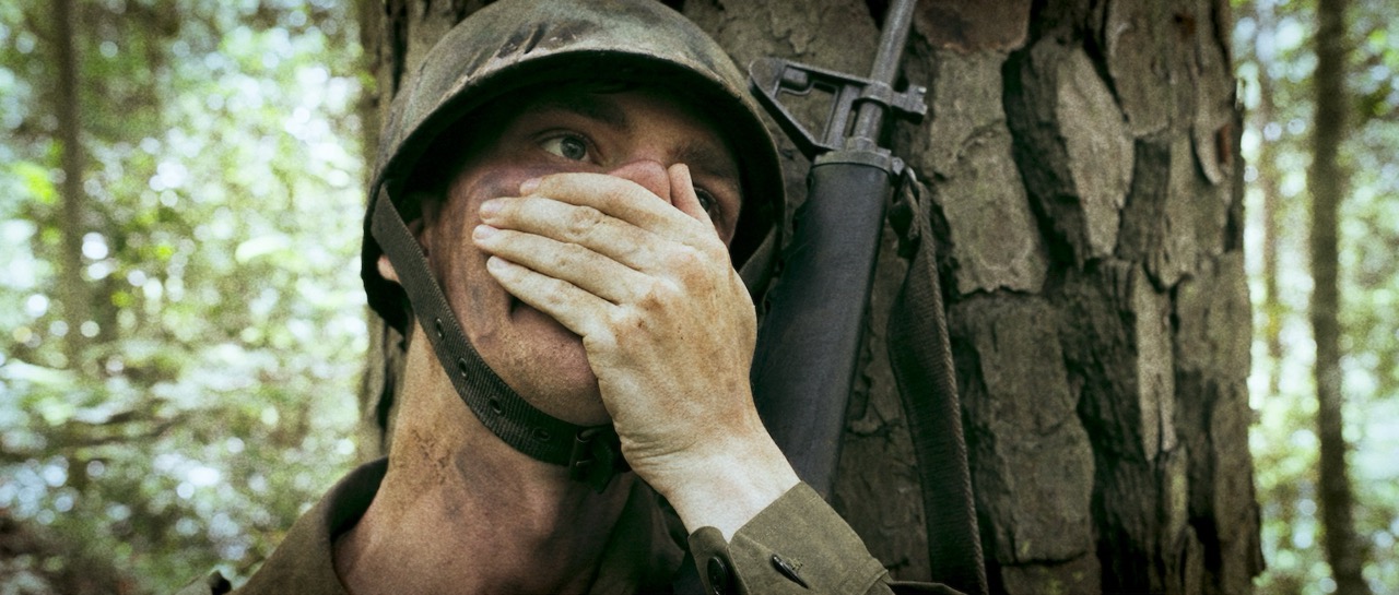 a man in a war uniform holds his breath as he leans against a tree