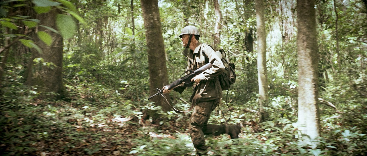 a man in a war uniform runs through a dense forrest