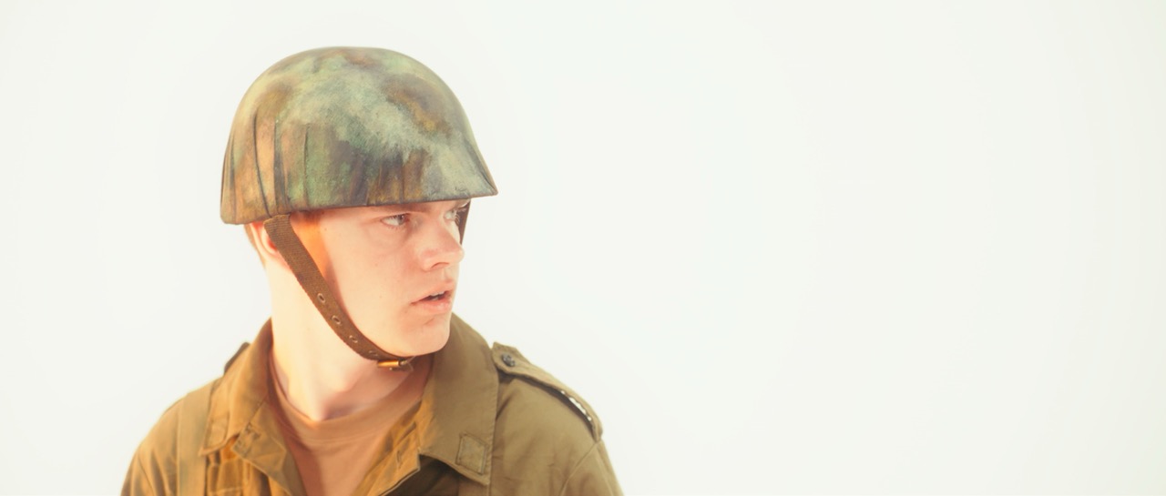 a man in a war uniform looks afraid in a white void, an orange glow hits his face