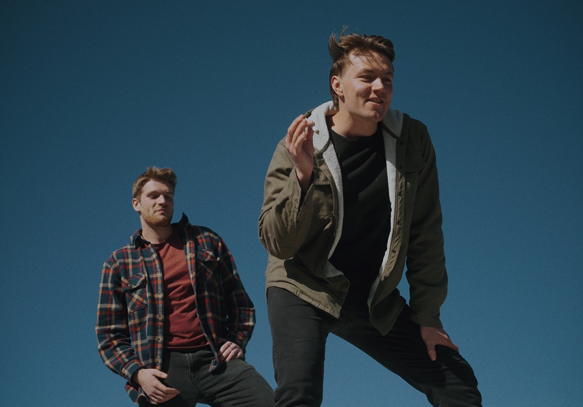 two young men stand against the sky