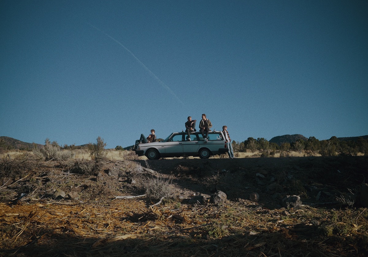 four boys rest against the side of the car on the top of a hill