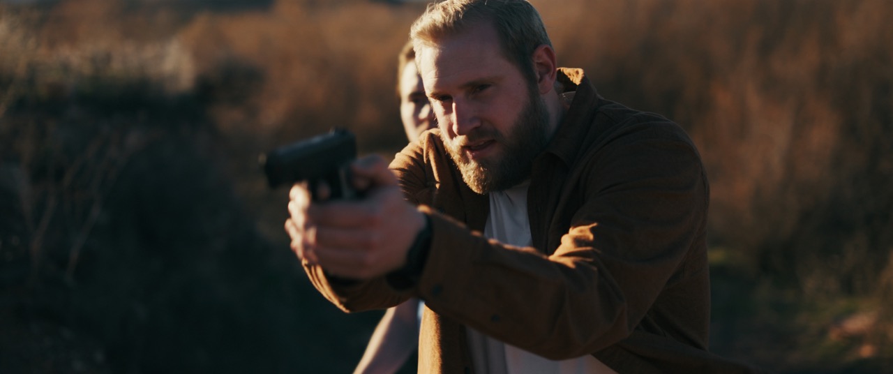 a man holds a gun to protect a man behind him
