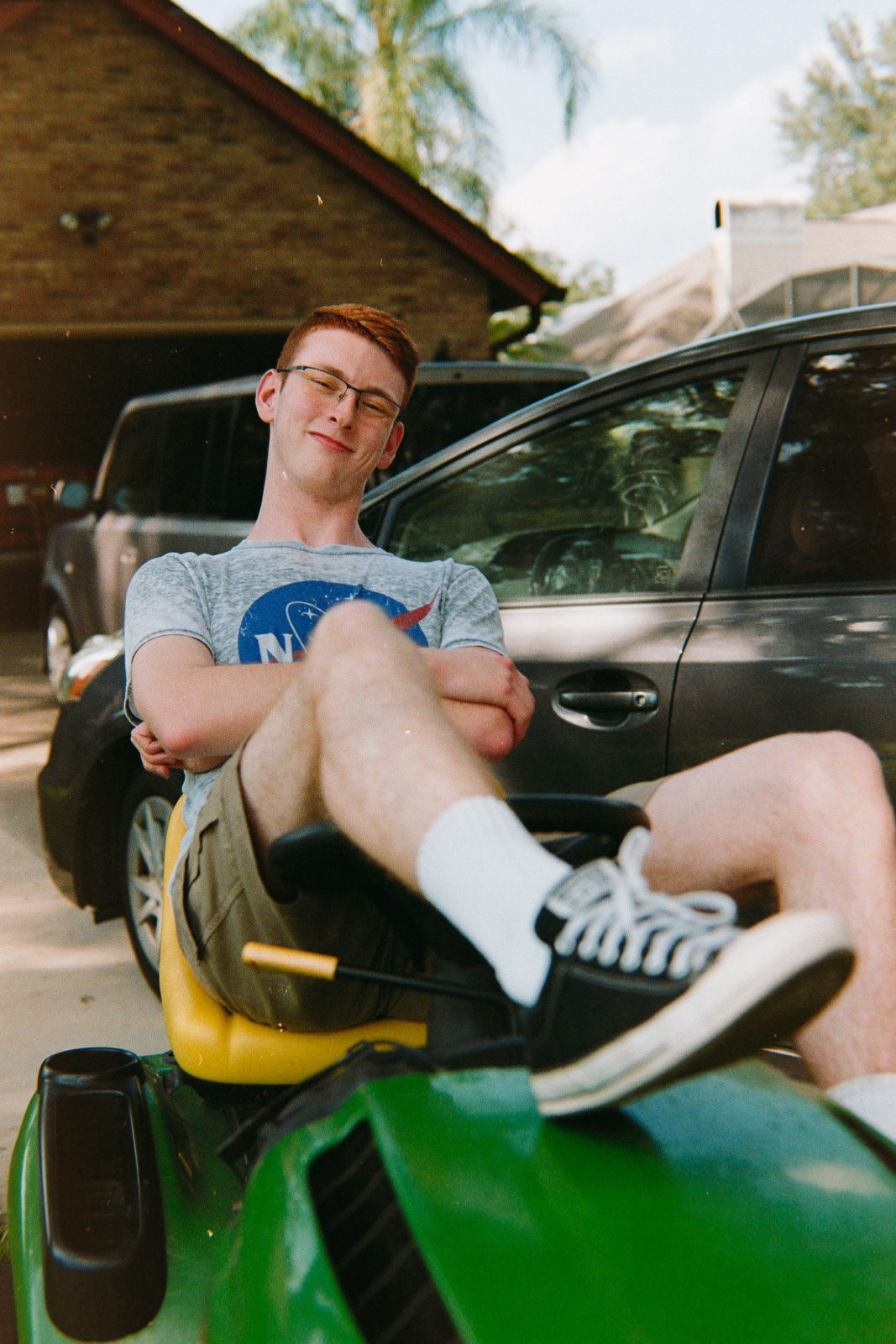 goofy portrait of a boy lounging on a riding lawn mower
