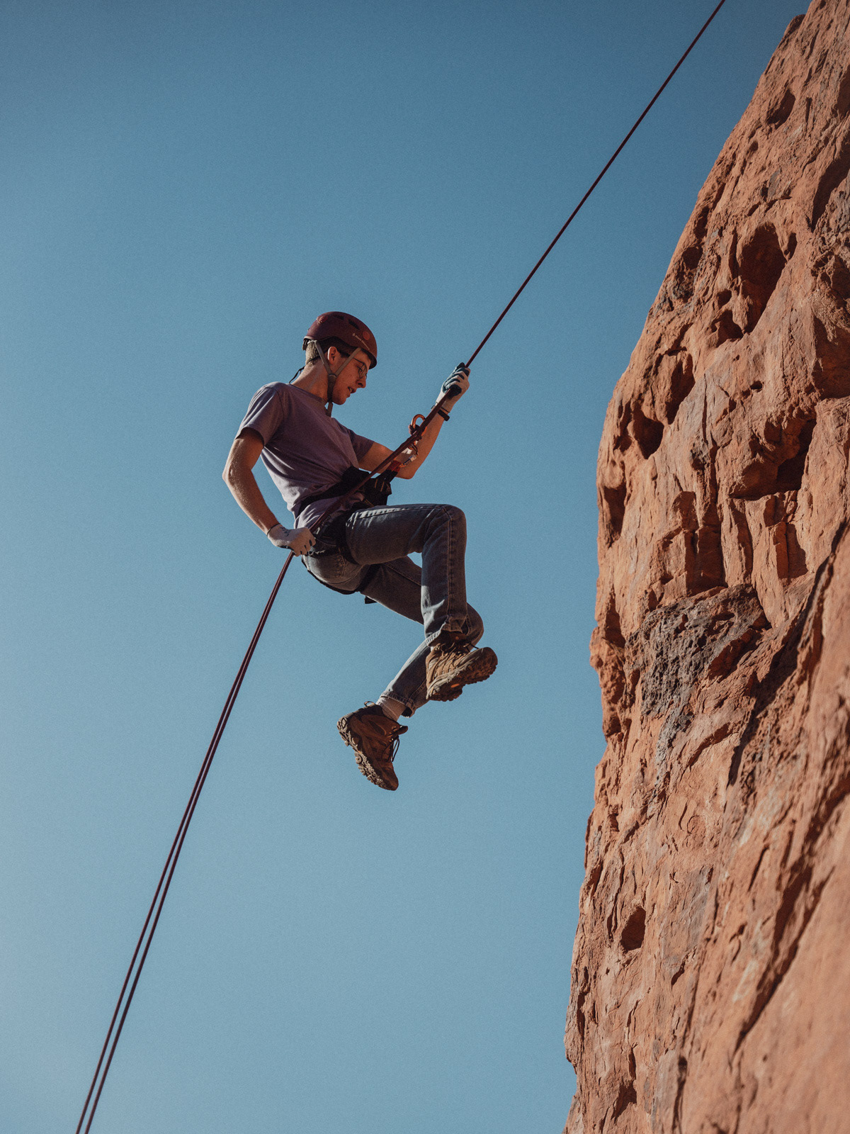 a man seemingly floating off the side of a red rock wall