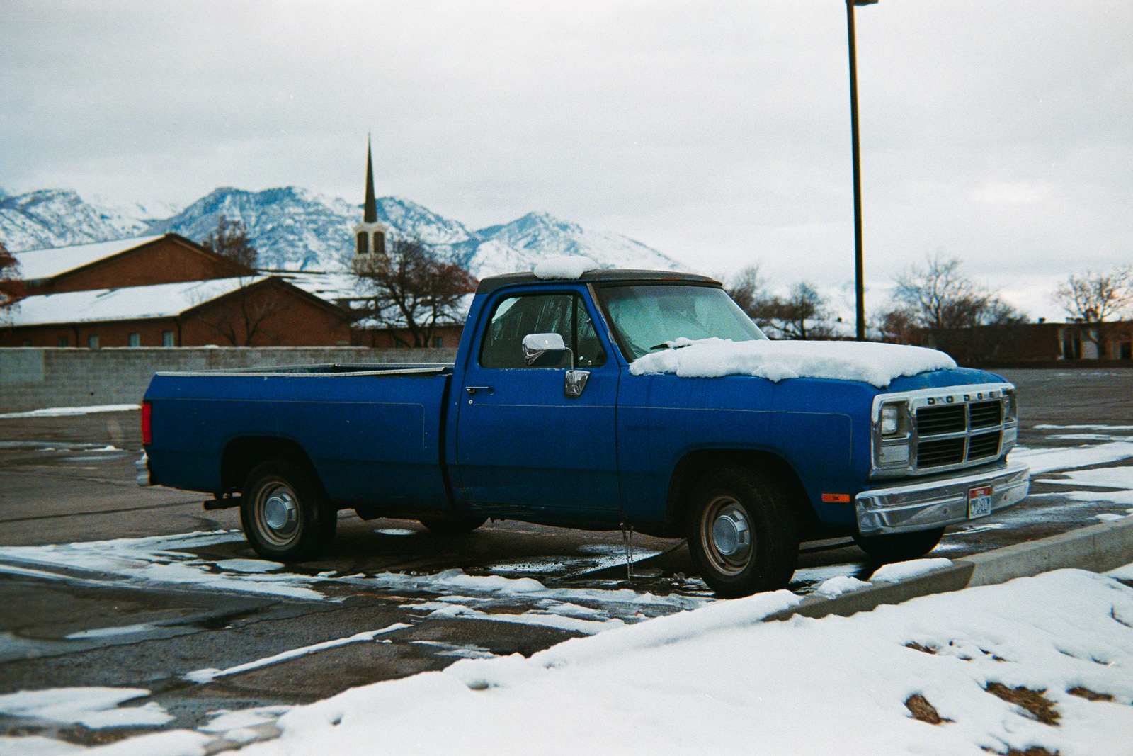 an old, blue, snow covered truck sits in an empty parking lot